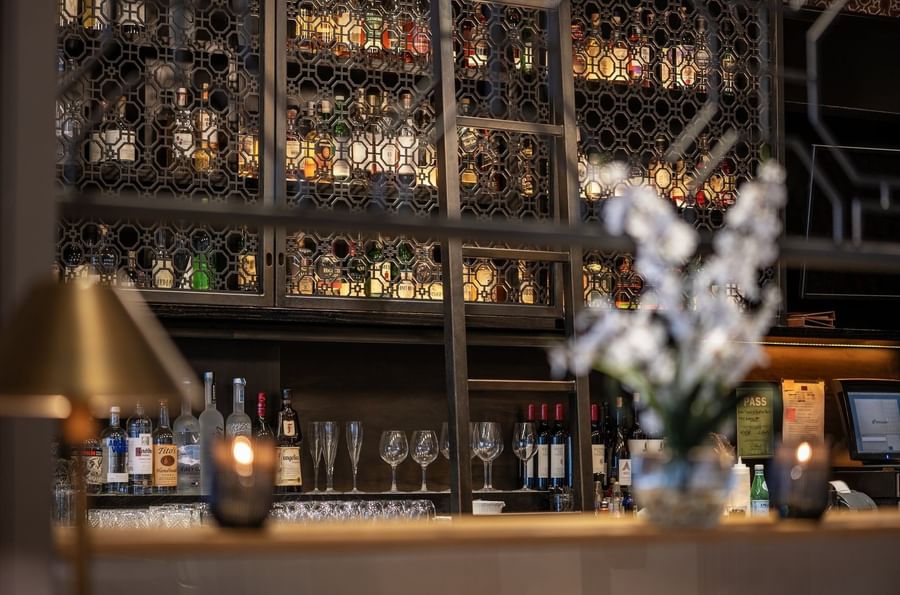 Liquor bottles on shelves behind a metal screen near glassware in The European at Warwick San Francisco
