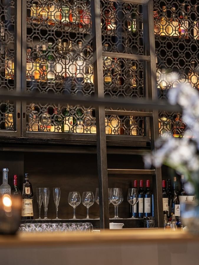 Liquor bottles on shelves behind a metal screen near glassware in The European at Warwick San Francisco