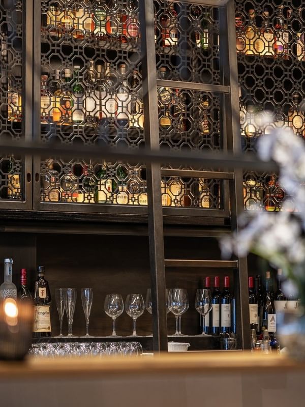 Liquor bottles on shelves behind a metal screen near glassware in The European at Warwick San Francisco