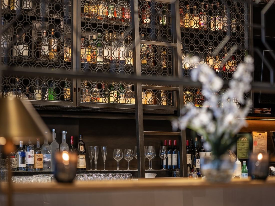Liquor bottles on shelves behind a metal screen near glassware in The European at Warwick San Francisco