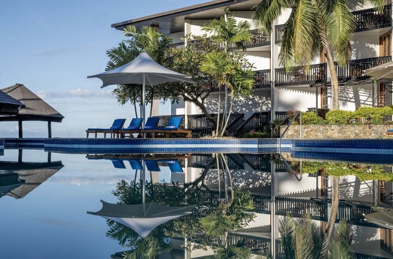 Resort pool with umbrellas and loungers reflecting on water at Warwick Fiji Resort and Spa