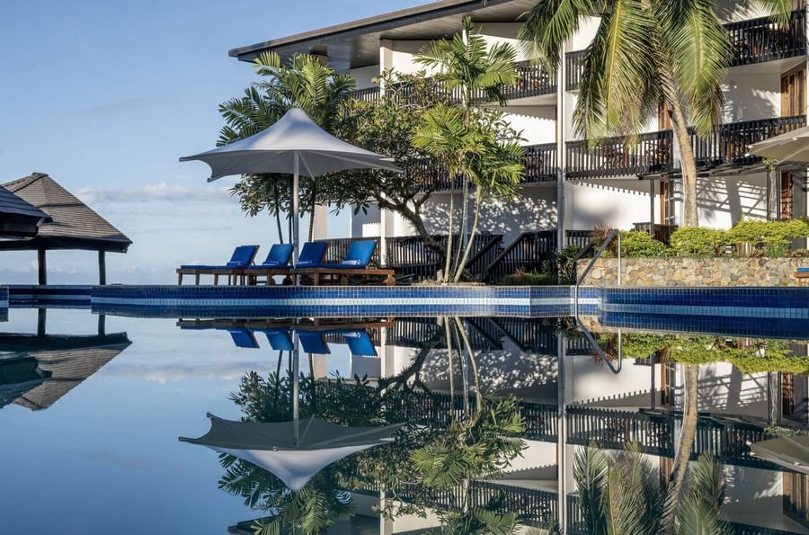 Reflective pool by blue loungers under a white umbrella near a balcony at Warwick Fiji Resort and Spa