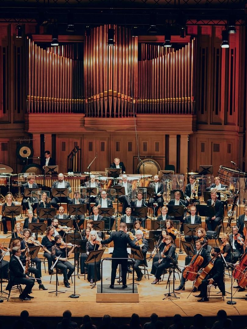 Orchestra and conductor on a wooden stage before a huge pipe organ in a concert hall near Warwick Brussels Grand-Place