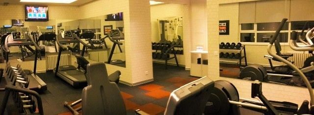Dumbbells on racks in a gym featuring mirrors and exercise bikes by white pillars at Warwick Ankara