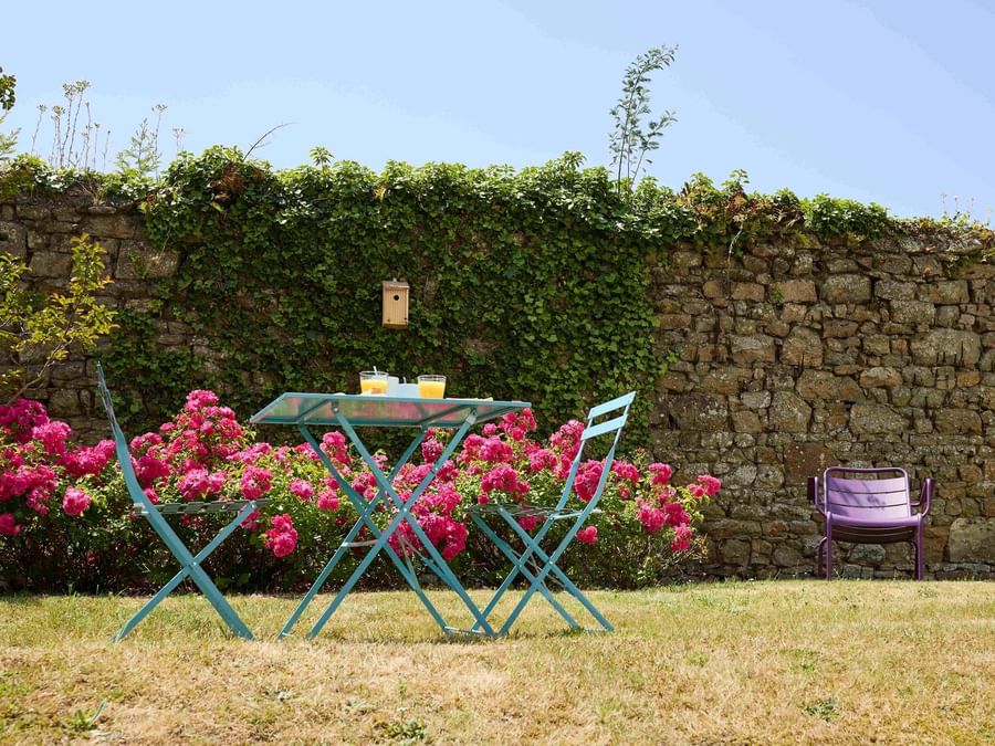 Table et chaises bleues dans un jardin fleuri devant un mur de pierres à Hôtel La Marébaudière.