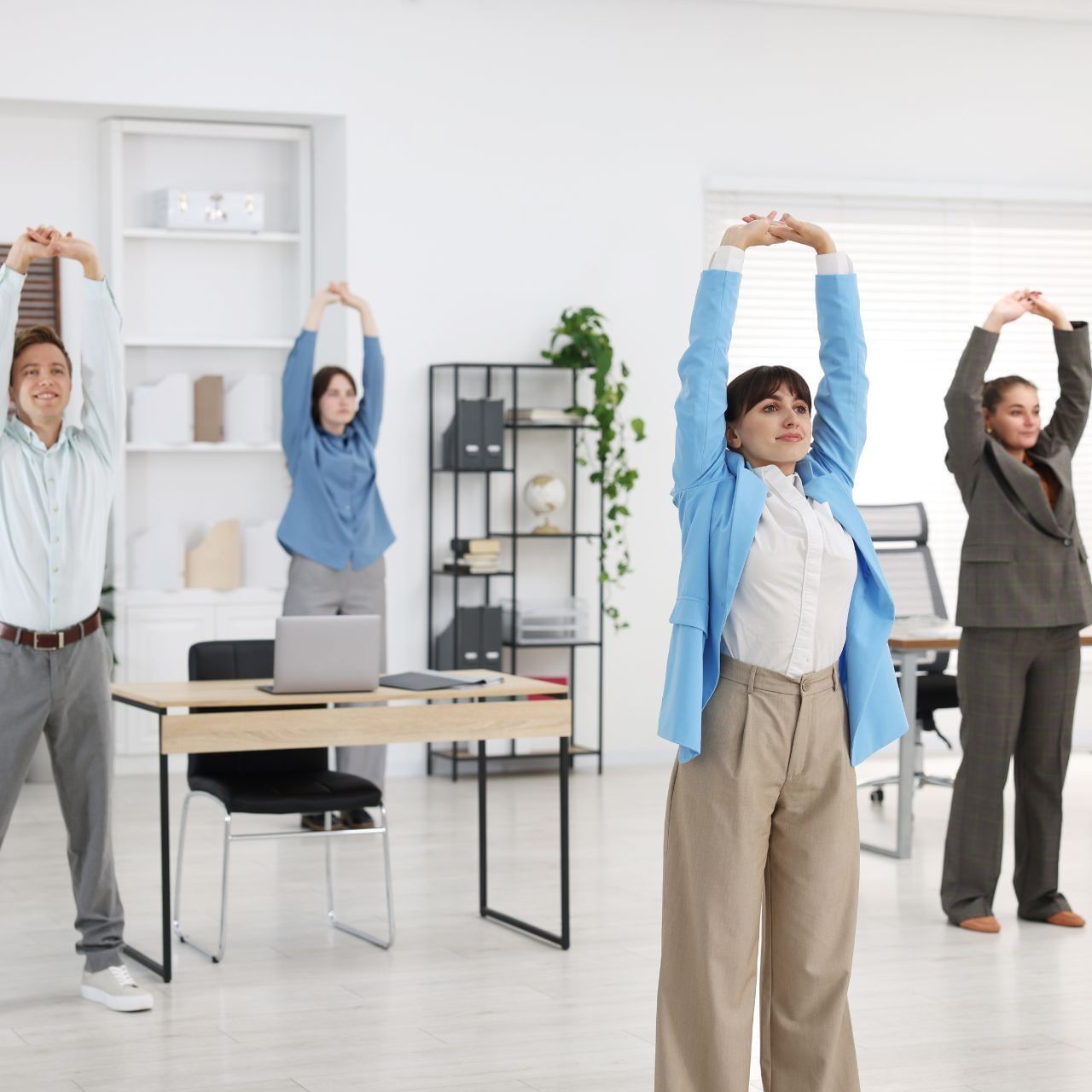 Four business professionals stretching with arms raised overhead in a bright modern office