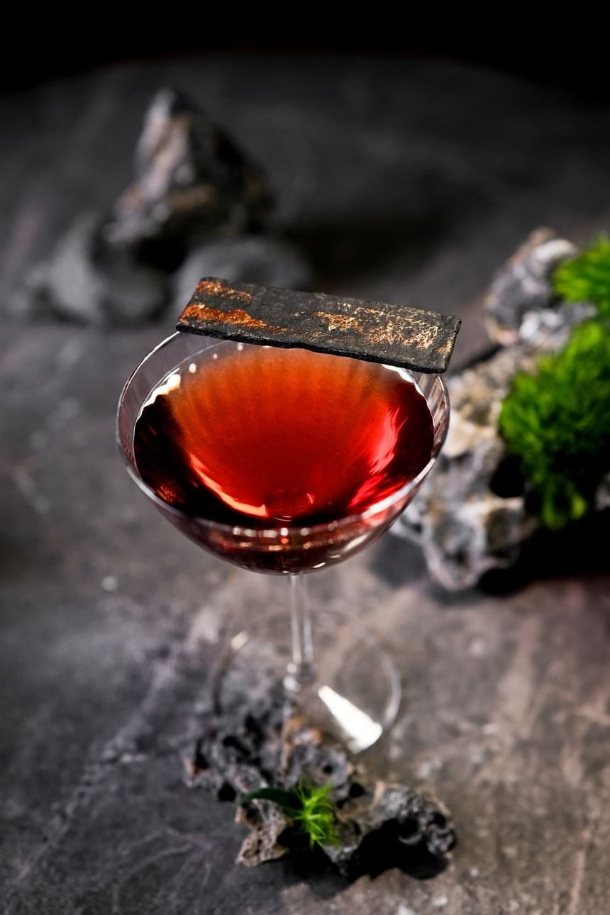Close-up of a red cocktail garnished with a dark textured piece on a stone in 2 Lams Son at Park Hyatt Saigon