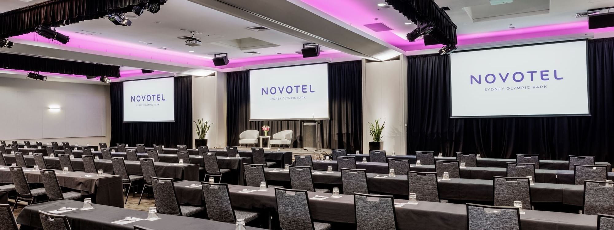 Classroom set-up with projector screens and purple lighting in Freshwater Ballroom at Novotel Sydney Olympic Park