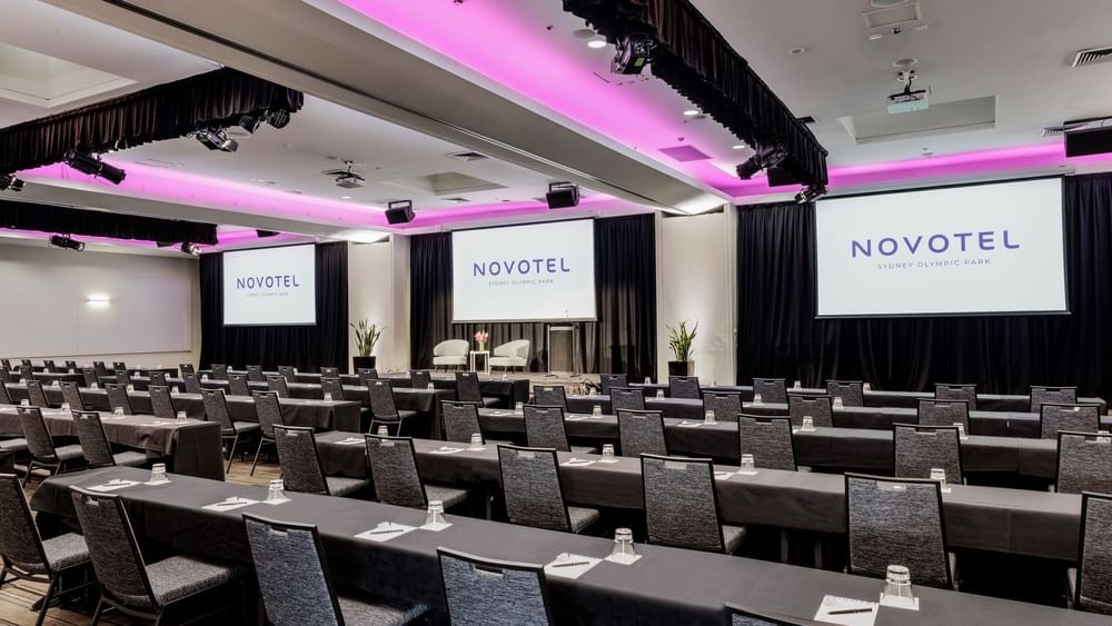 Classroom set-up with projector screens and purple lighting in Freshwater Ballroom at Novotel Sydney Olympic Park