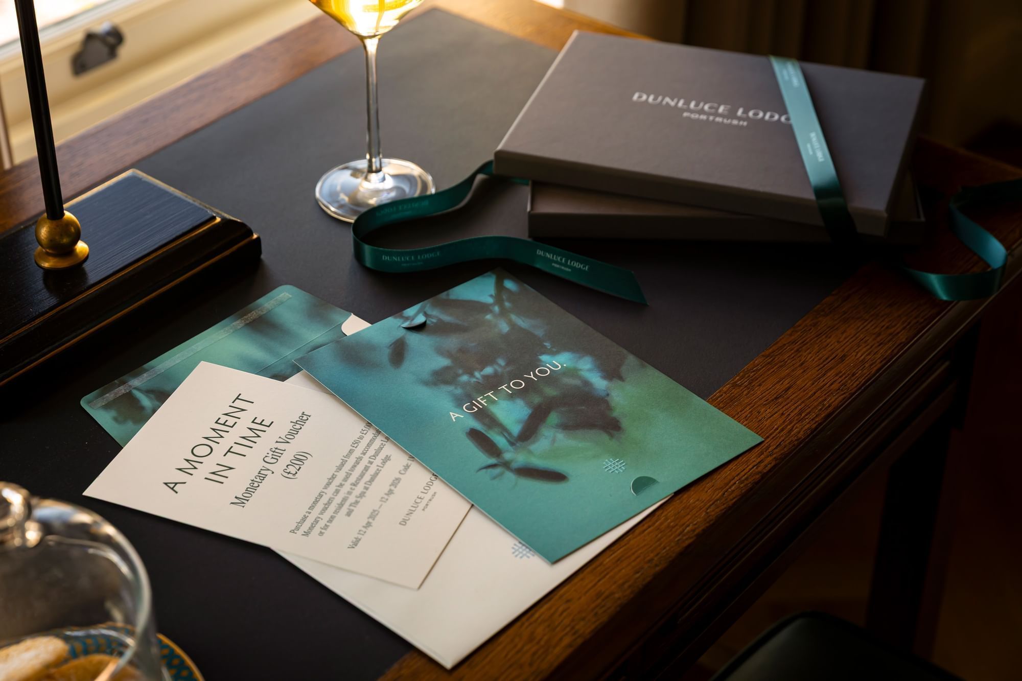 A close-up of a gift box and vouchers from Dunluce Lodge, with a cocktail on a dark wooden desk