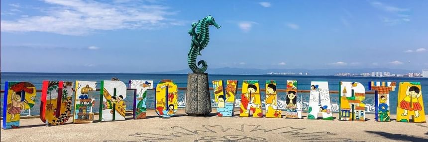 The iconic bronze seahorse statue next to the colorful Puerto Vallarta sign on a sunny beach boardwalk near Casa Dona Susana