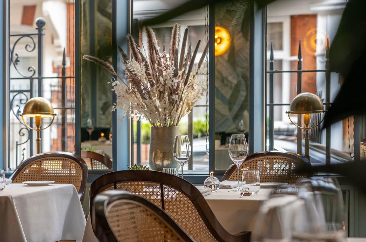 Dining table with chairs by large windows under a dried floral arrangement at The Capital Hotel, Apartments and Townhouse