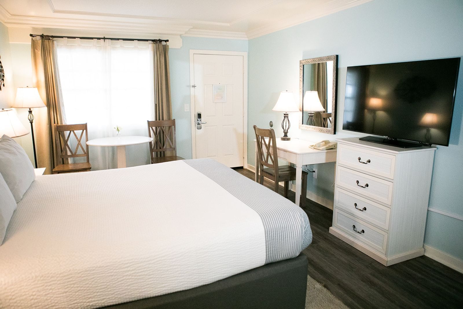 A hotel room with a king-sized bed, TV, desk, and window
