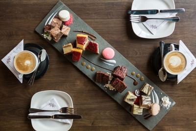Bandeja de postres junto a tazas de café bajo luz suave sobre mesa de madera en el café de NOI Vitacura