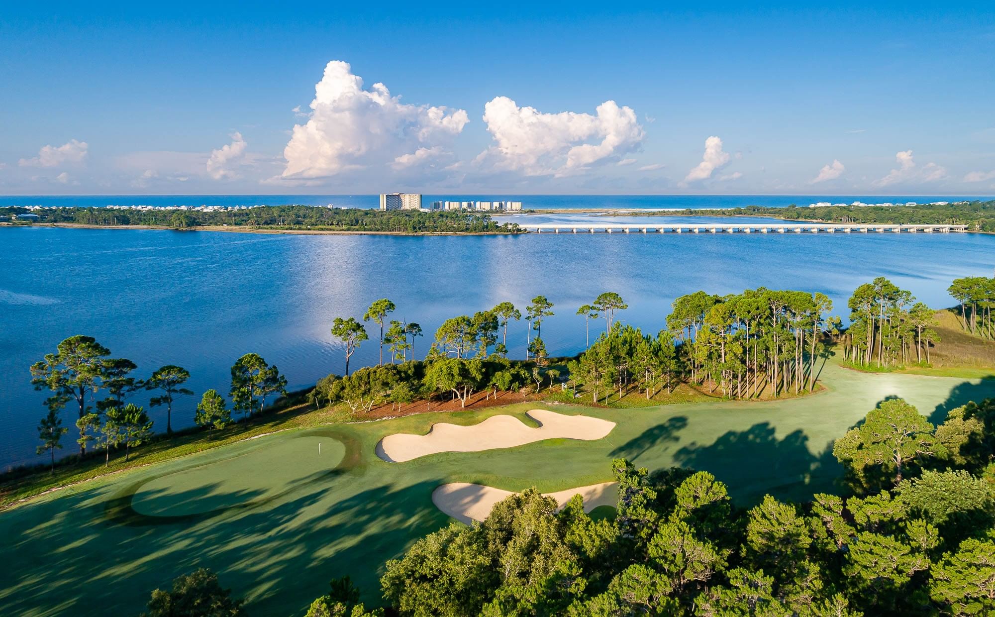 Aerial view of Shark's Tooth Golf Course with water views and buildings in the distance.