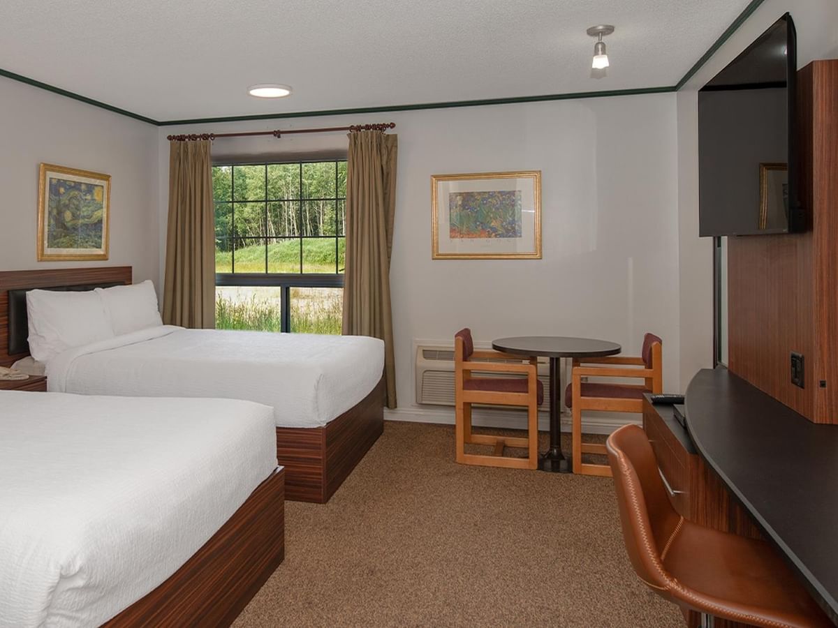 Guest room with two queen beds, a work desk, wall-mounted TV and window