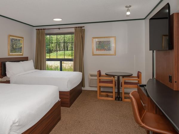 Guest room with two queen beds, a work desk, wall-mounted TV and window