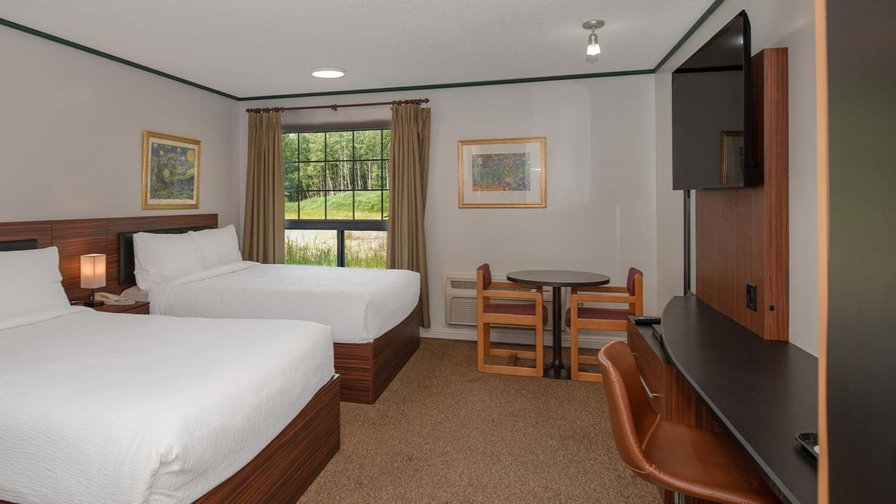 Guest room with two queen beds, a work desk, wall-mounted TV and window