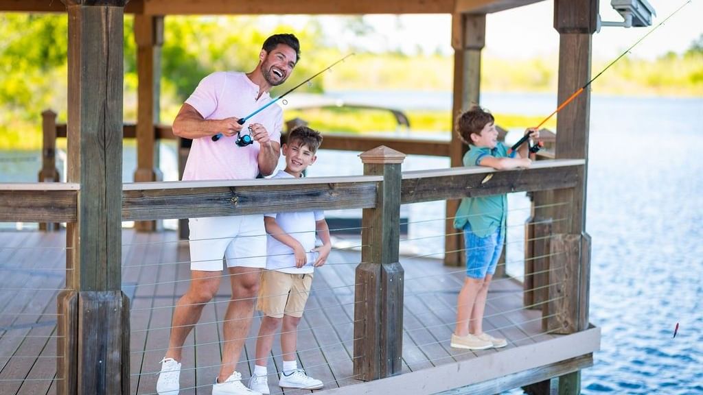 Father and two children enjoying sunrise fishing together on a wooden lakeside dock with fishing rods in hand
