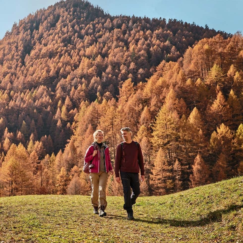 Zwei Wanderer auf einem Bergpfad vor einer beeindruckenden herbstlichen Bergkulisse.