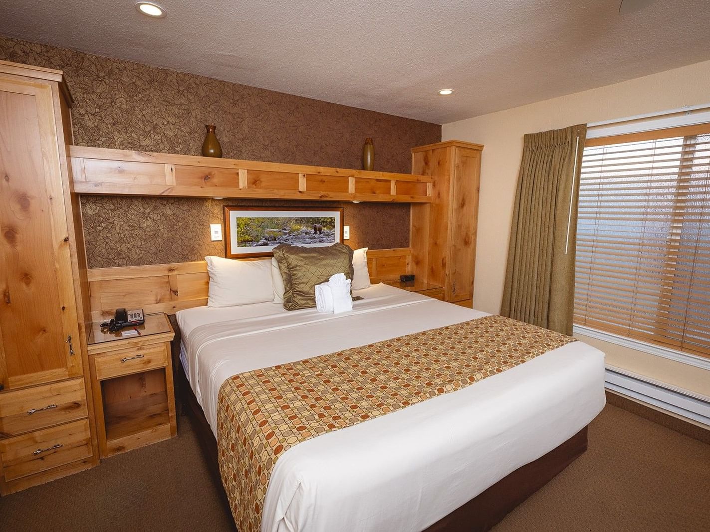 Deluxe One Bedroom Suite provide a welcoming view with a queen bed and a yellow quilted comforter at Americana Village Suites