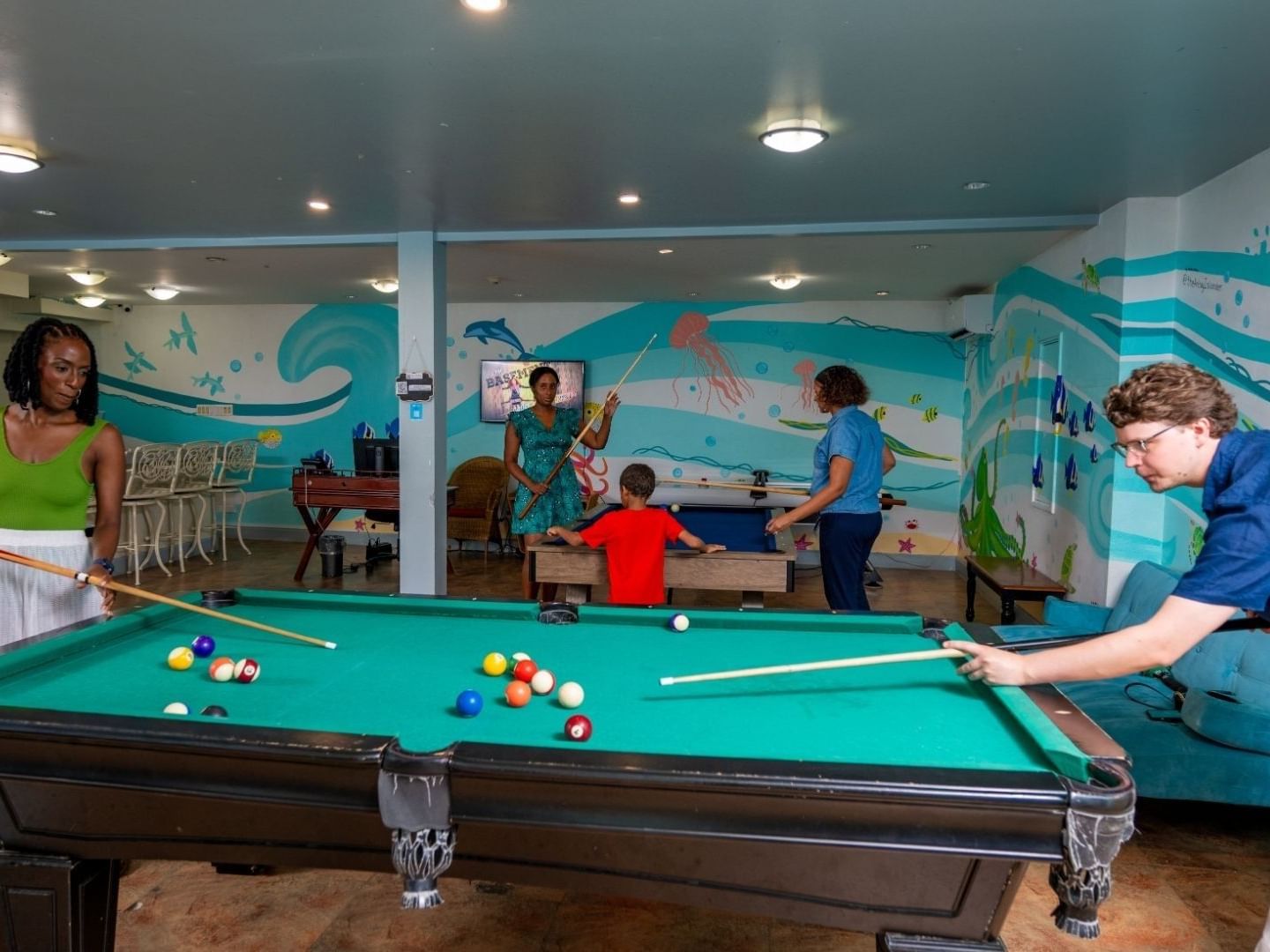 People playing pool in a game room with marine life murals at Savannah Beach Hotel.