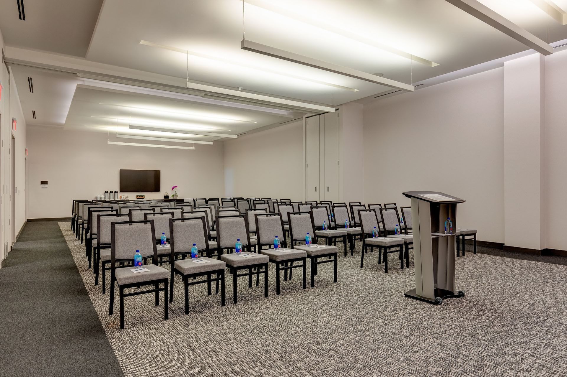 Riverdale set up room with rows of gray chairs facing a podium and screen under linear lights at Hotel X Toronto