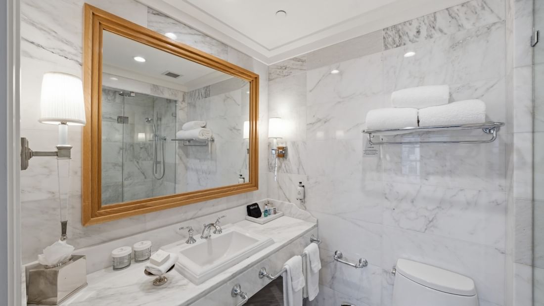 Elegant marble bathroom with glass shower, wood-framed mirror, and white towels in Courtyard Grand Executive King Suite at el PRADO Hotel.