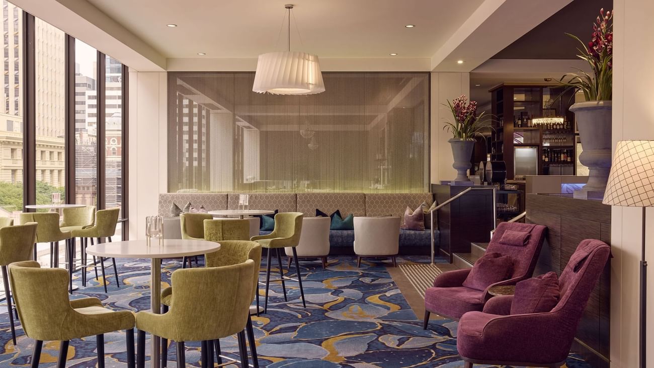 Modern lounge with green chairs, armchairs and city view in Cuvée at Sofitel Brisbane Central