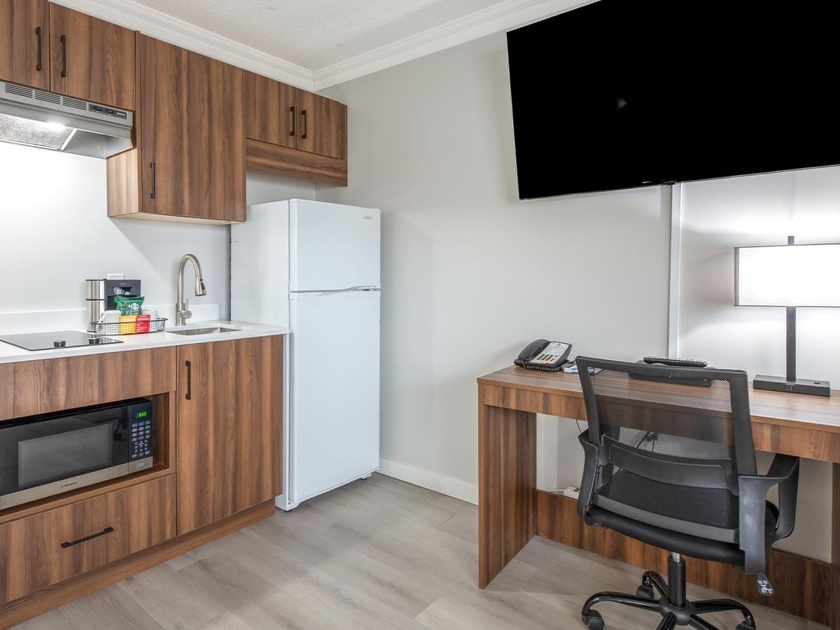 A kitchenette with a fridge, microwave, and coffee maker, as well as a desk and chair.