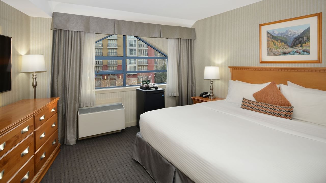 Spacious hotel room with a king bed, elegant decor and large window for natural light.