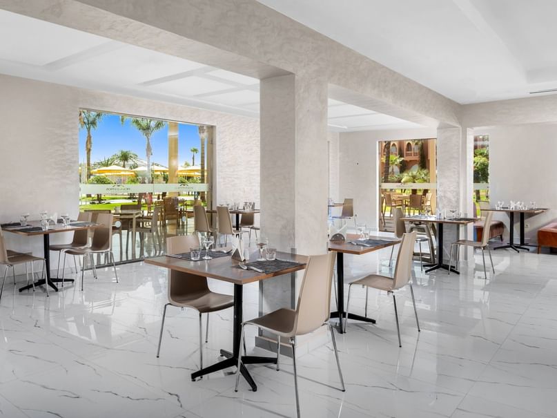 An elegant dining room with set tables, glass walls, and large windows showing an outdoor patio.