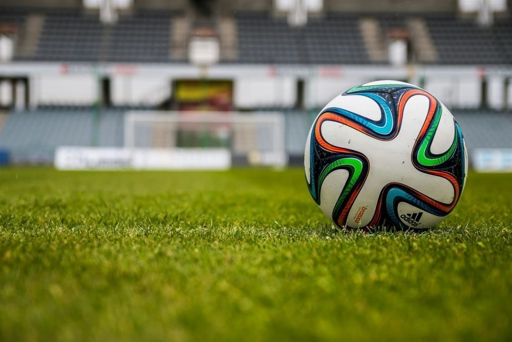 A colorful soccer ball resting on grass with an empty out-of-focus arena in the background.