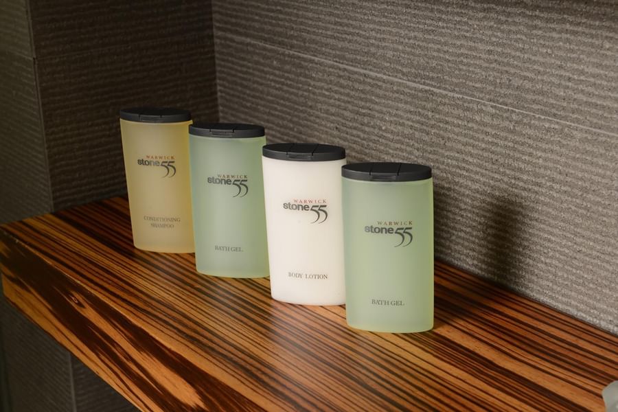 Bottles of shampoo and lotion by a grey wall on a wood-grain shelf in Deluxe Room at Warwick Stone 55 - Beirut