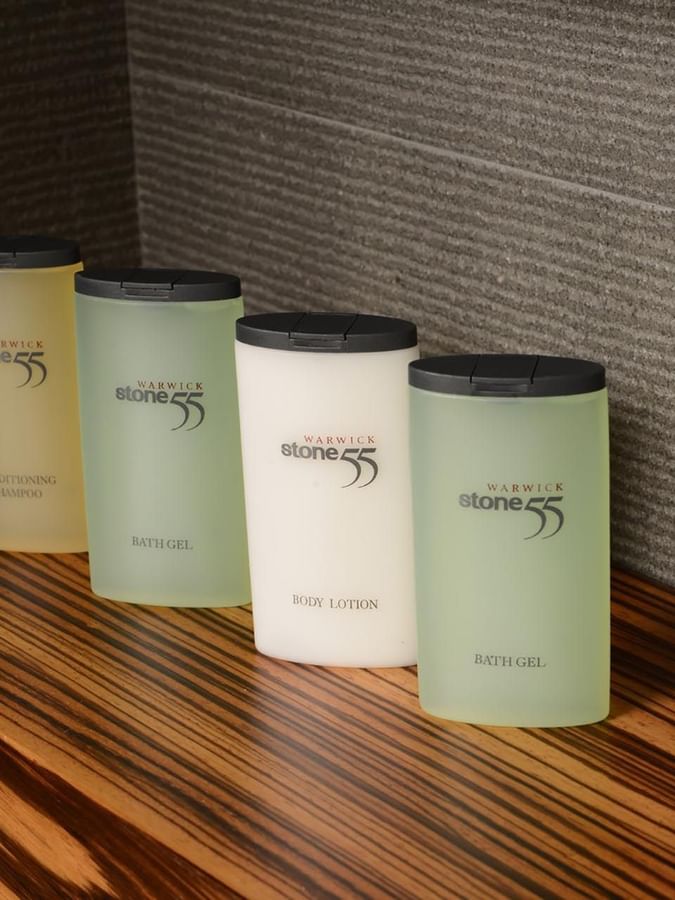 Bottles of shampoo and lotion by a grey wall on a wood-grain shelf in Deluxe Room at Warwick Stone 55 - Beirut