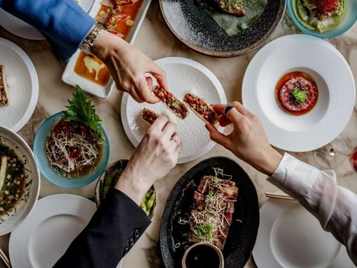 Overhead view of diners sharing colorful Gyoza Tacos on various plates in May Fair Kitchen