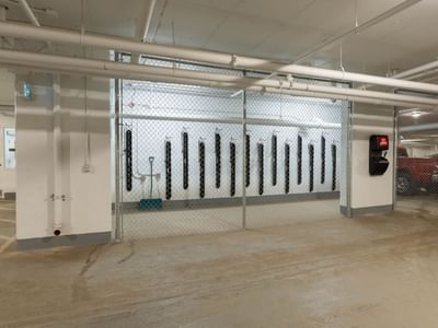 A bike storage area secured by a chain link gate sits in a bright and well-lit underground parking garage.