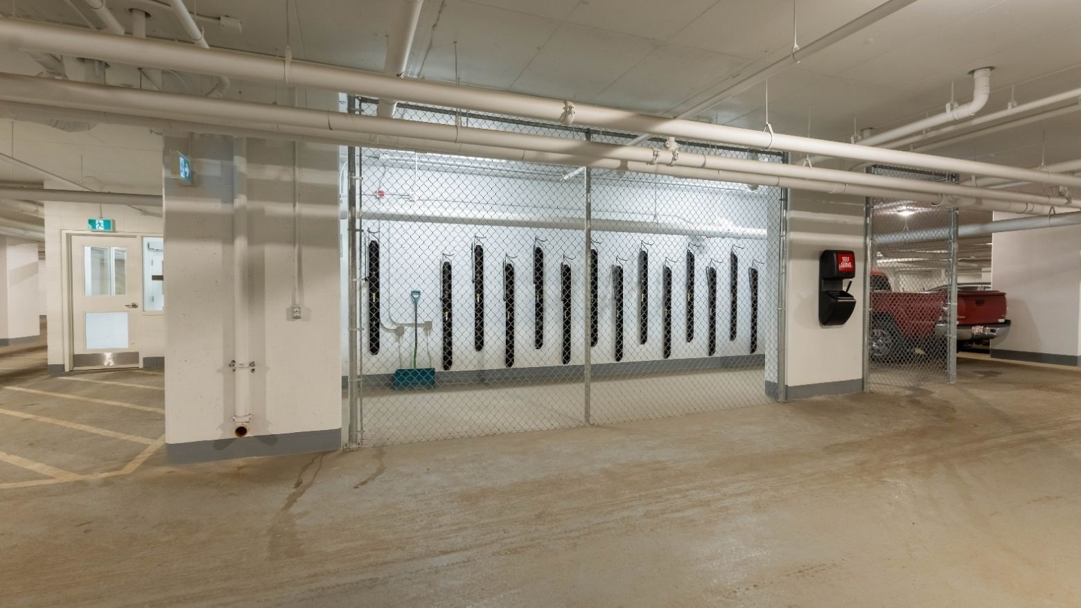 A bike storage area secured by a chain link gate sits in a bright and well-lit underground parking garage.