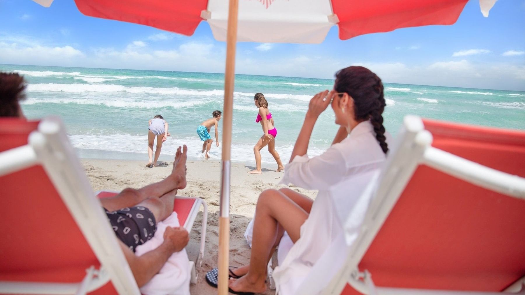 A family enjoying the beach & sitting under an umbrella at The Diplomat Resort