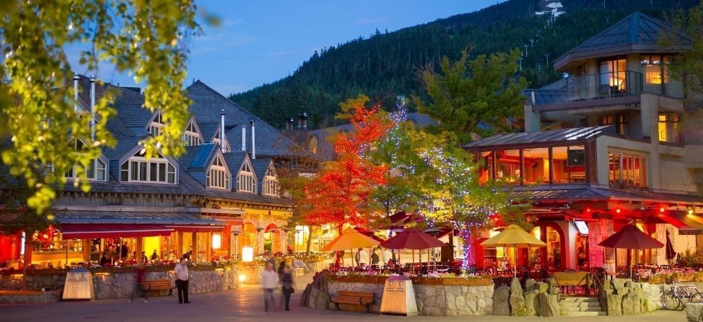 Evening view of Whistler Village with vibrant shopfronts, patios, and illuminated trees.