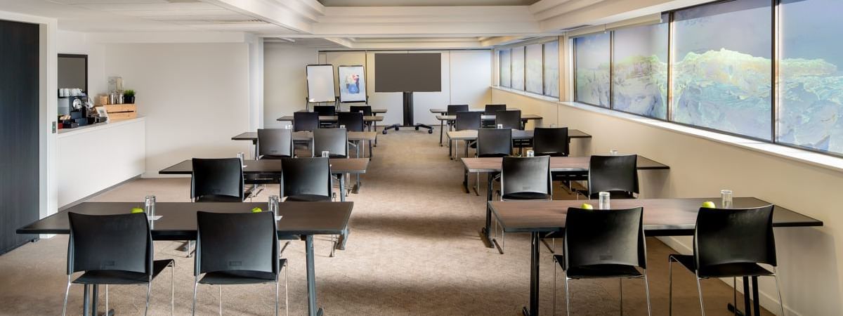 Classroom table setup facing the projector screen by the large windows in Acacia at Novotel Sydney International Airport