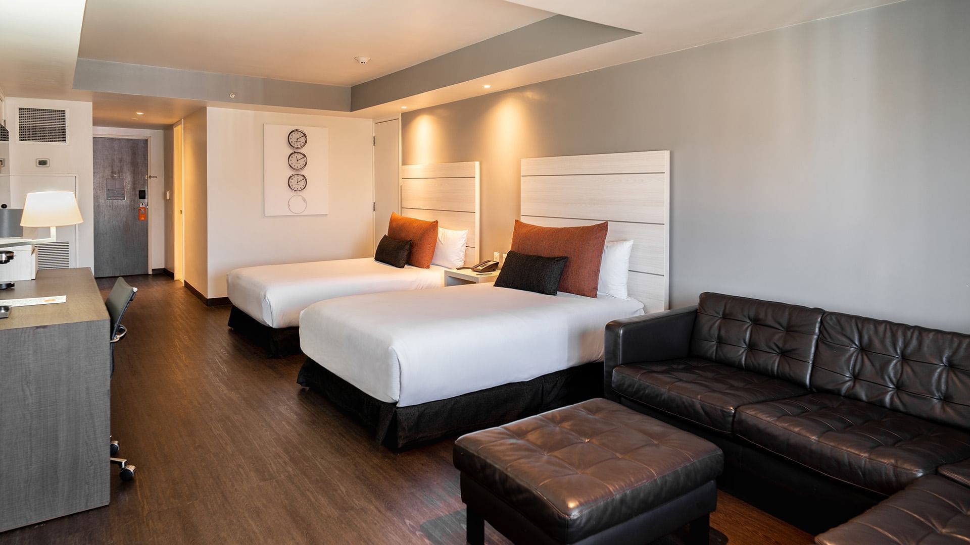 Nightstand and a dark tufted leather sofa by the cozy bed in Two Double Junior Suite at Real Inn Tijuana