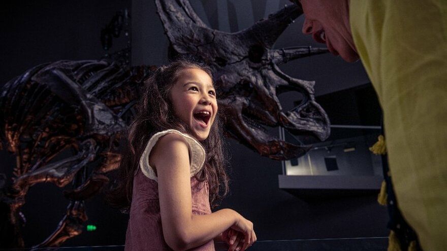 Melbourne Museum little girl smiling infront of fossil dinosaur skeleton