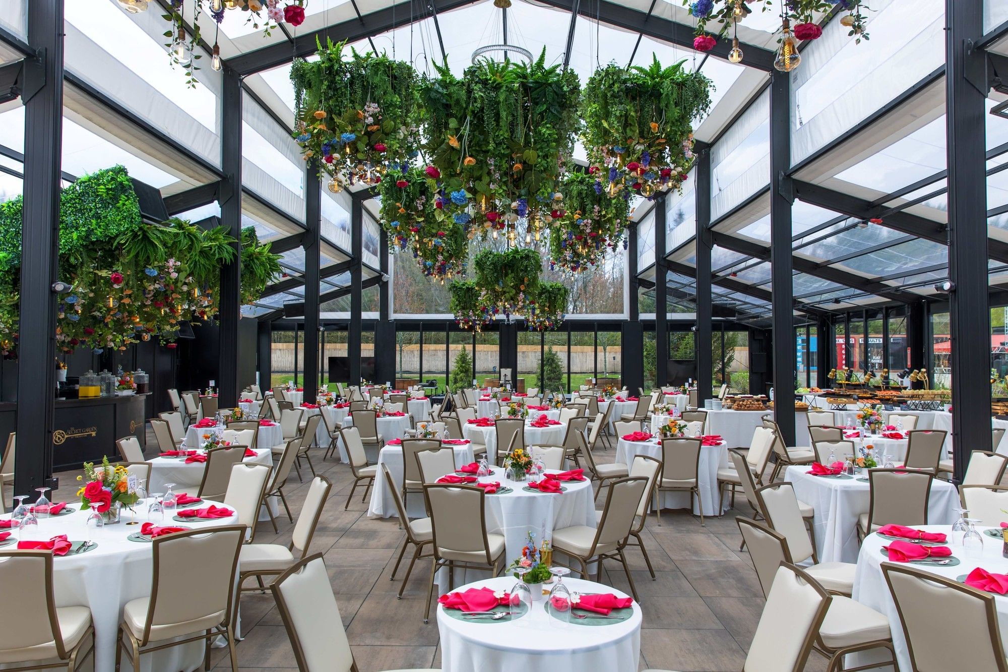 Round white-clothed tables with pink napkins by cream chairs under chandeliers in The Secret Garden Brunch at The Brook
