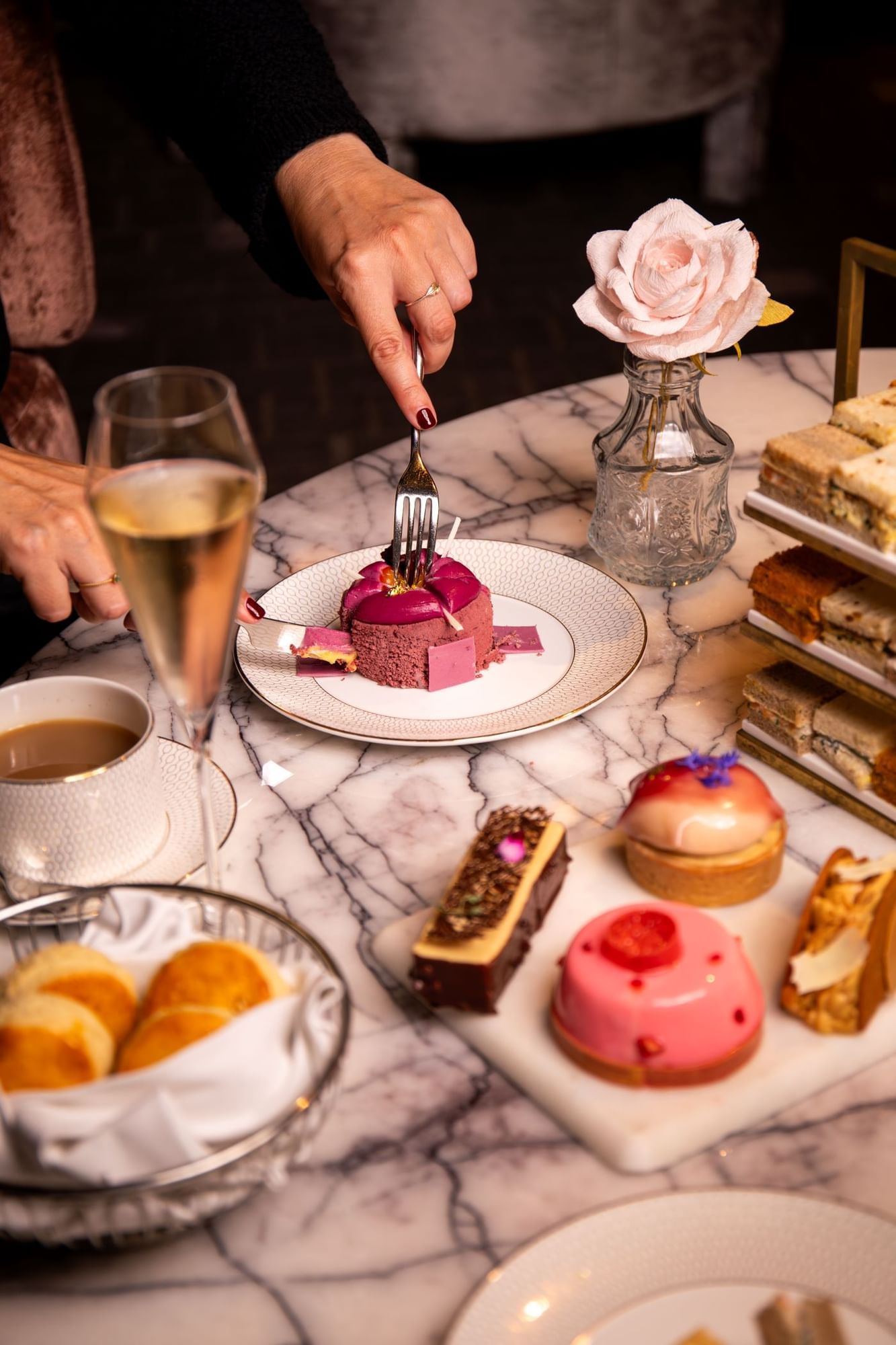 A person cutting into a vibrant purple dessert during an elegant afternoon tea experience at The Londoner Hotel