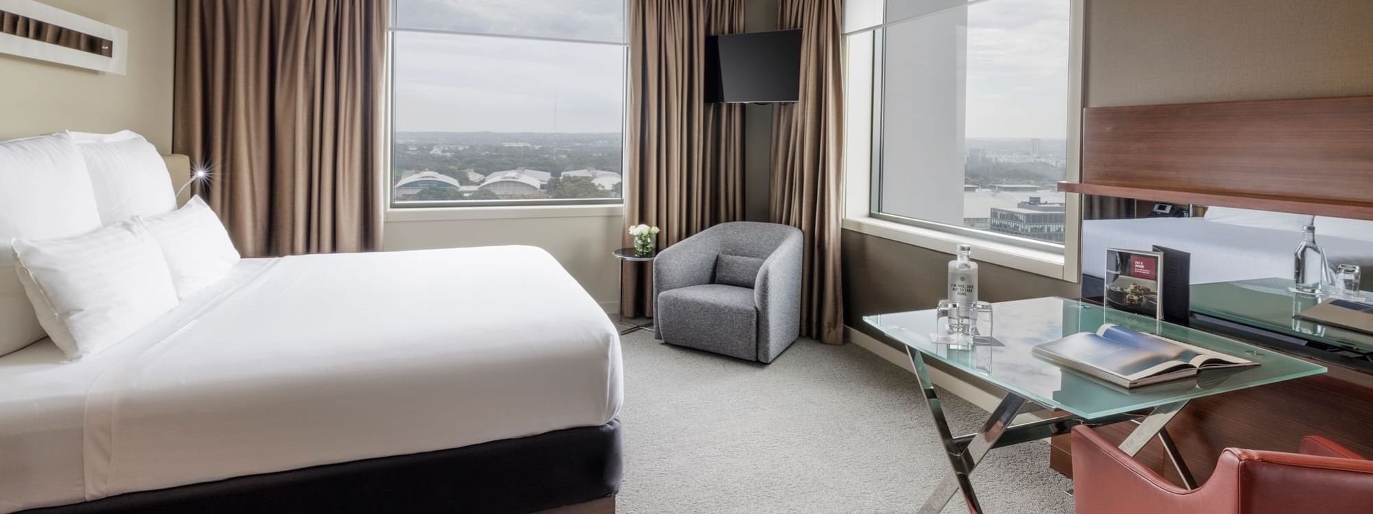 Wall-mounted TV with couch facing bed by the windows in Pullman Deluxe King Room at Pullman Sydney Olympic Park