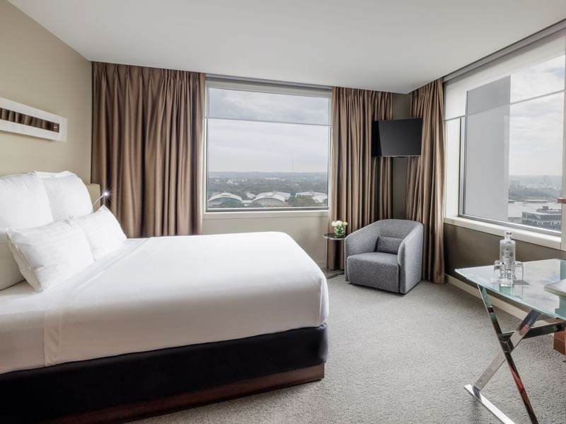 Wall-mounted TV with couch facing bed by the windows in Pullman Deluxe King Room at Pullman Sydney Olympic Park