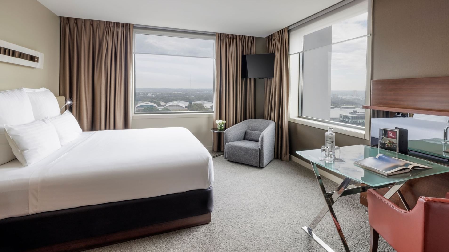 Wall-mounted TV with couch facing bed by the windows in Pullman Deluxe King Room at Pullman Sydney Olympic Park