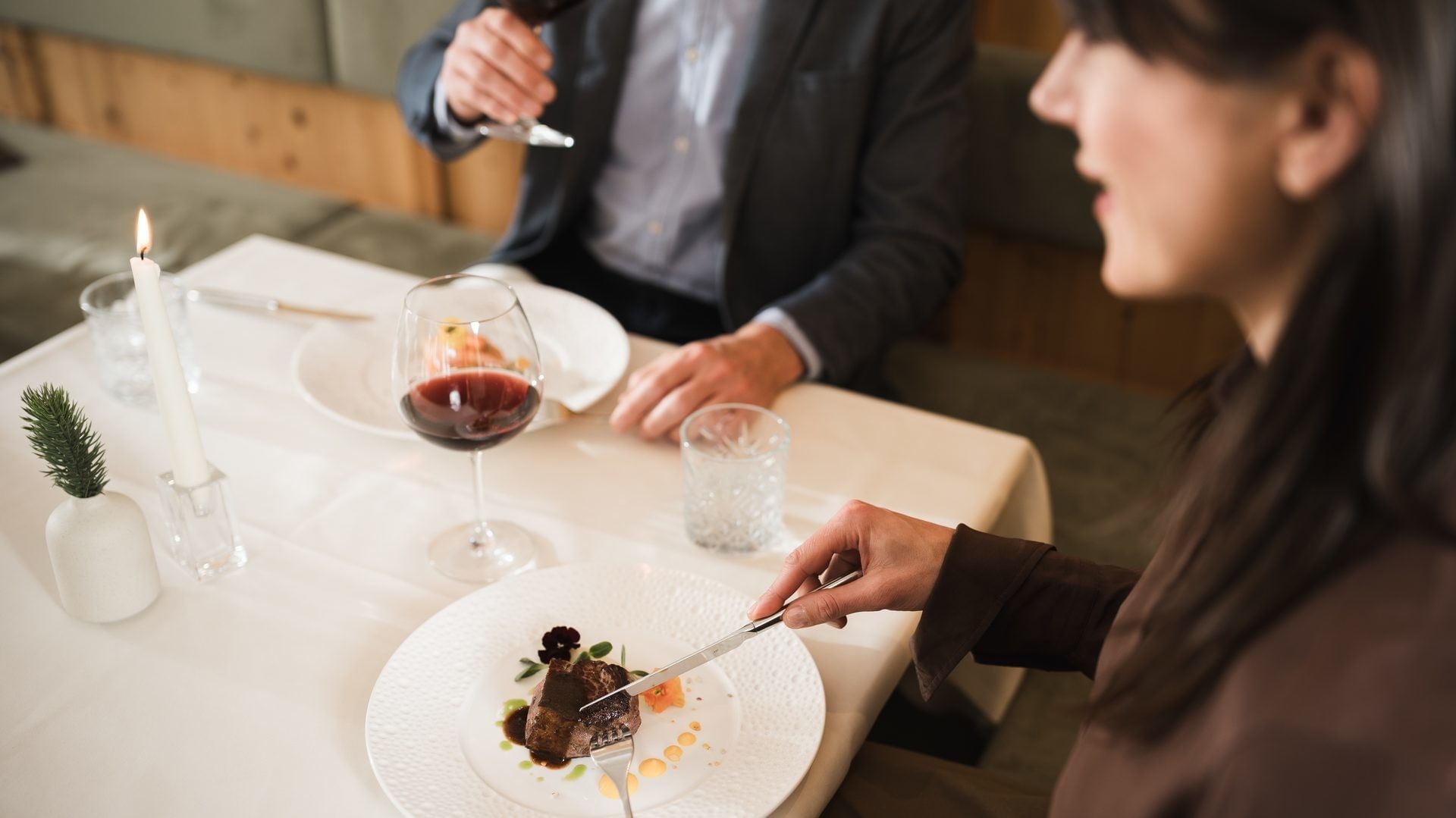 Frau schneidet Fleisch auf ihrem Teller während ein Mann Wein trinkt bei Falkensteiner Hotel Falkensteinerhof