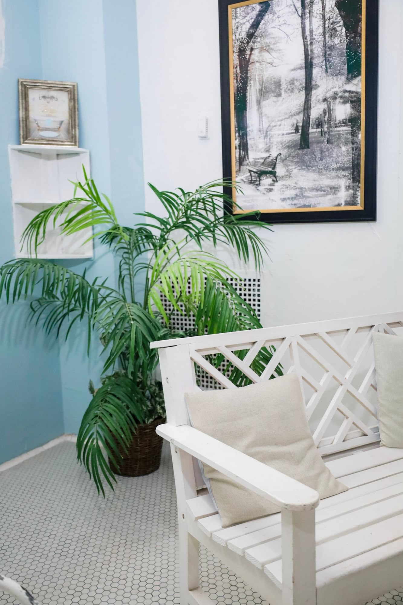 White wooden bench with beige cushions beside potted palms under framed artwork at Arlington Resort Hotel & Spa
